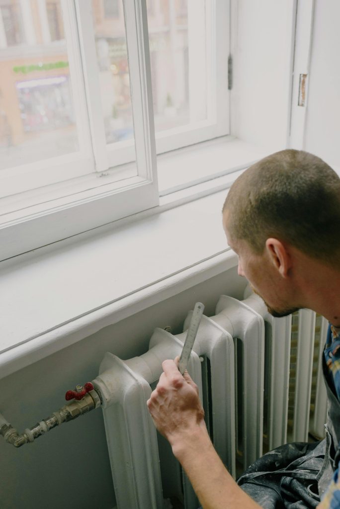 Unrecognizable handyman with ruler near heating system at home